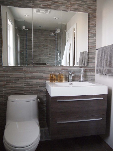 Mur sur lequel est installé un lavabo avec des meubles en bois, des toilettes et un grand miroir. Tuiles dans différentes nuances de brun et gris