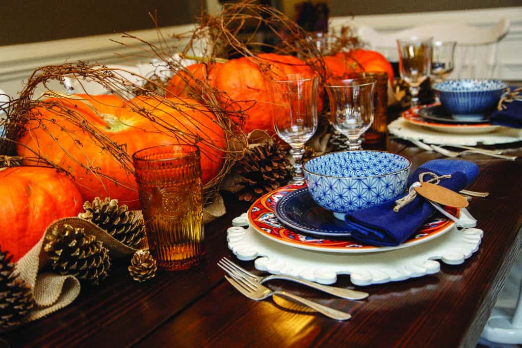 Table de thanksgiving enveloppée de branches de citrouilles et de pommes de pin