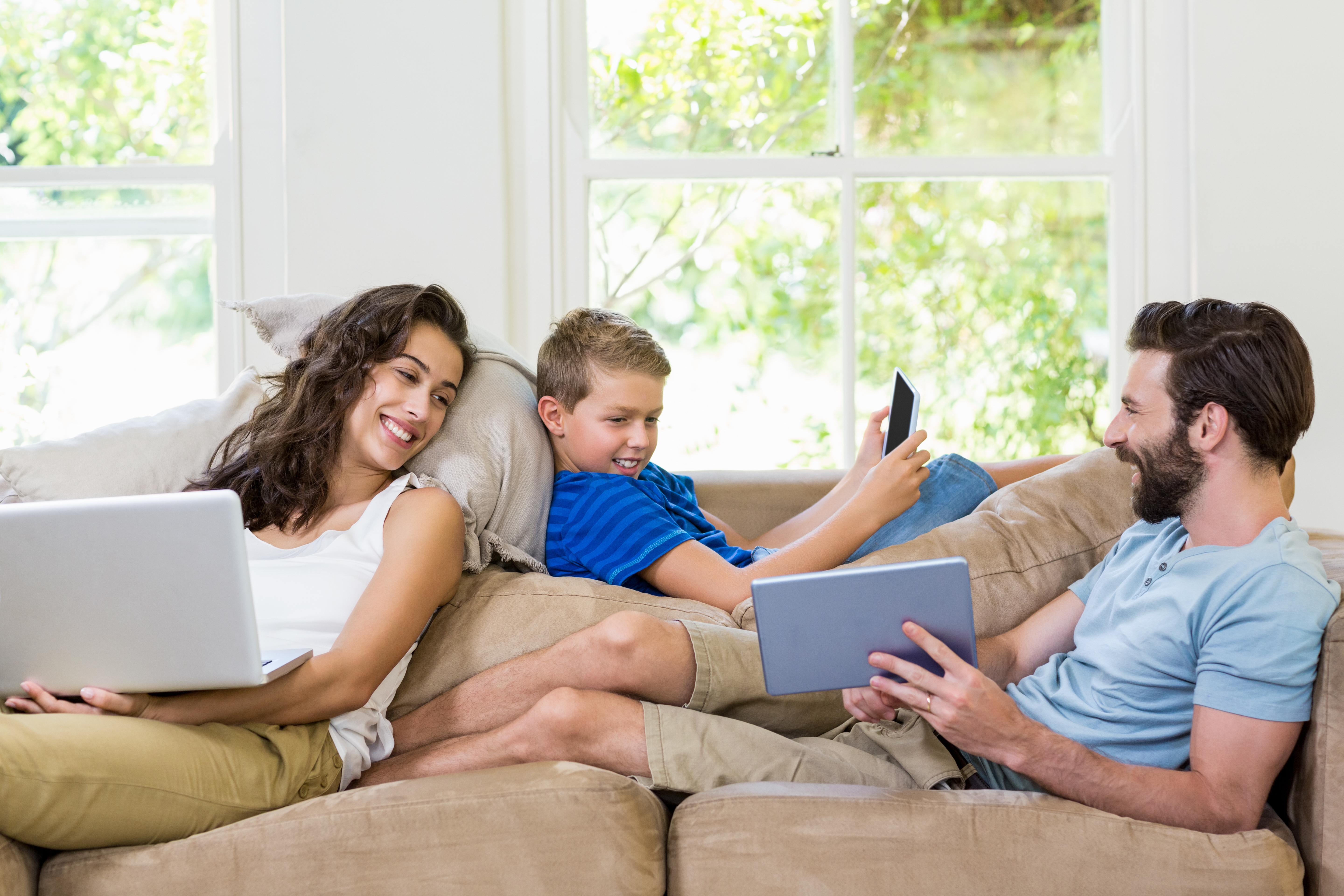 parents et enfant assis ensemble sur un canapé à l'aide de trois appareils différents