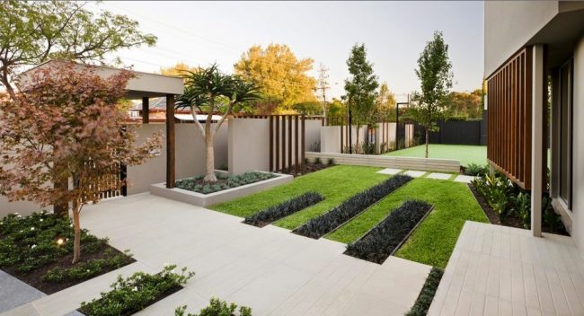 modern innergård omgiven av murar, med gångvägar i betong och gröna växtbäddar